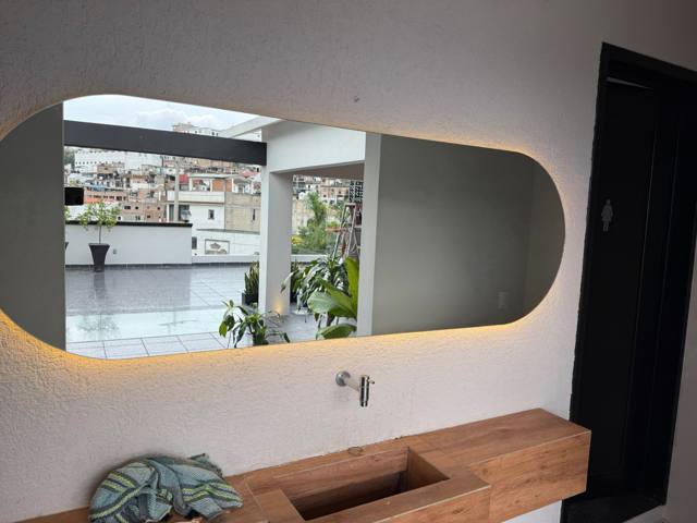 Espejo con luz perimetral cálida sobre lavabo de madera